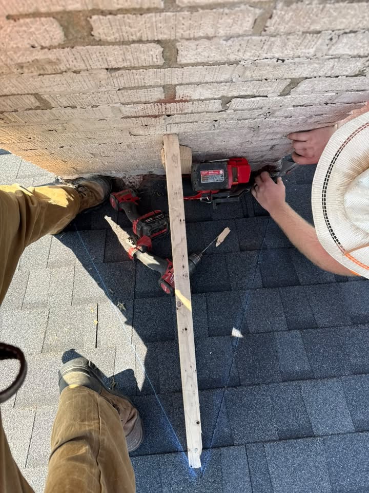 Roofing tools and new shingles laid along a brick wall during roof work